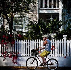 Man riding bicycle in Key West with wooden house and fence in view