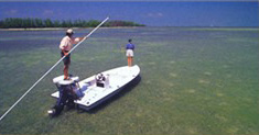 Flats fishing guide pushes skiff with pole while angler casts